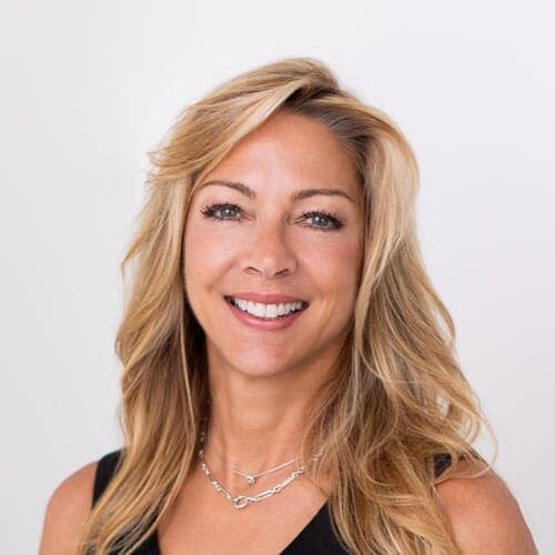 A woman with long blonde hair and a black top smiles at the camera against a plain white background.